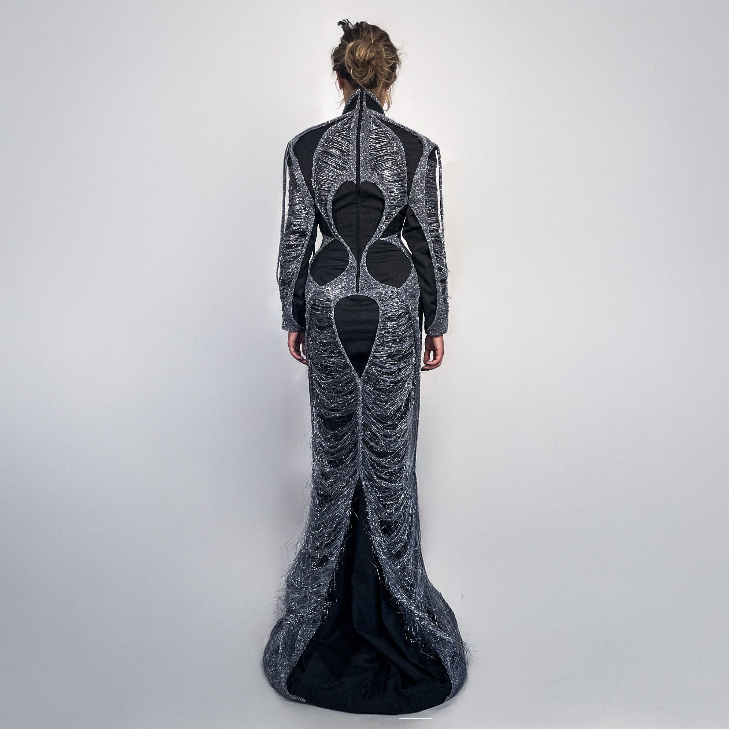 Woman wearing a long, dark gray dress layered with metallic knit on a light gray background 