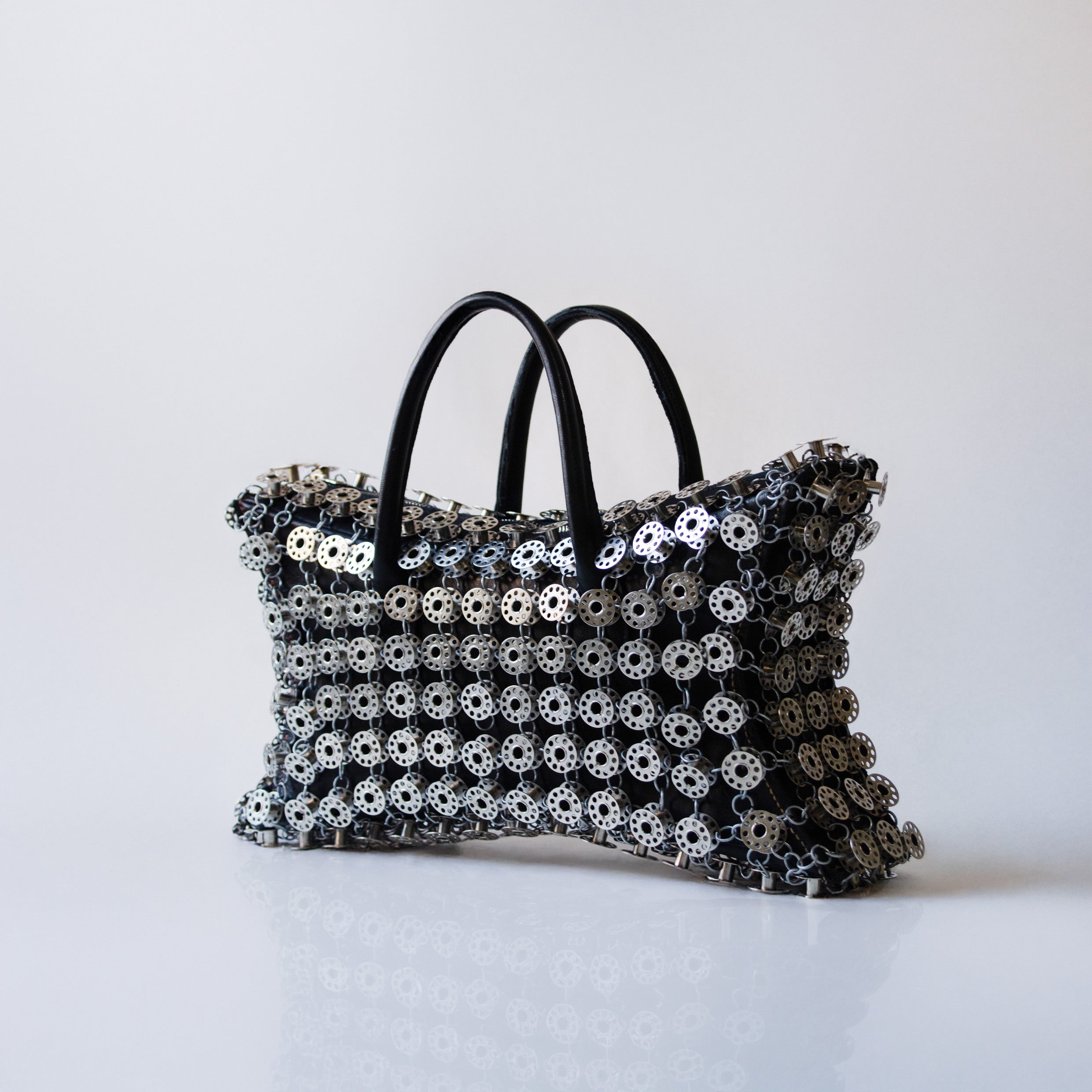 black leather star shaped handbag layered with metal bobbins on light gray background 