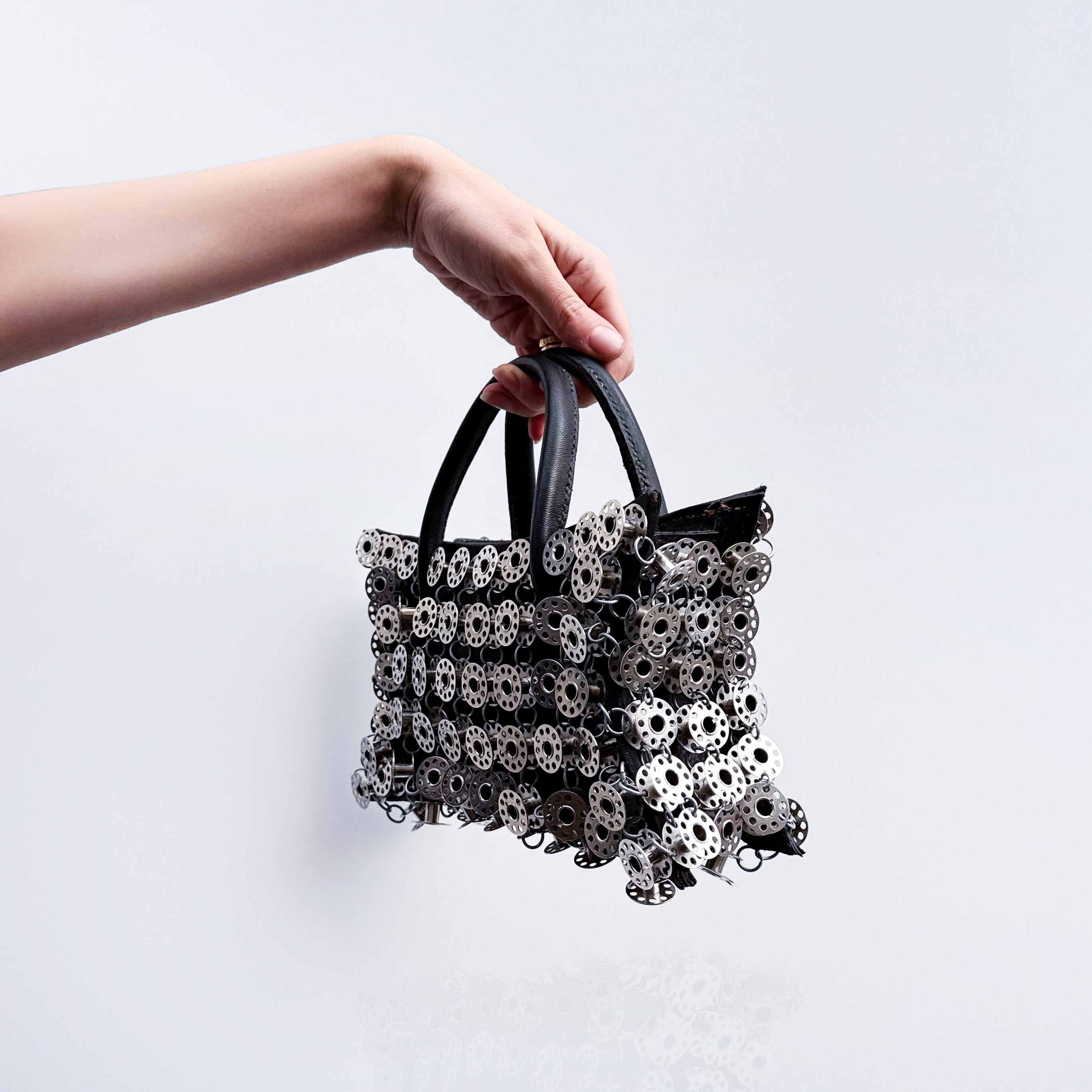 small black leather star shaped handbag layered with metal bobbins on light gray background 