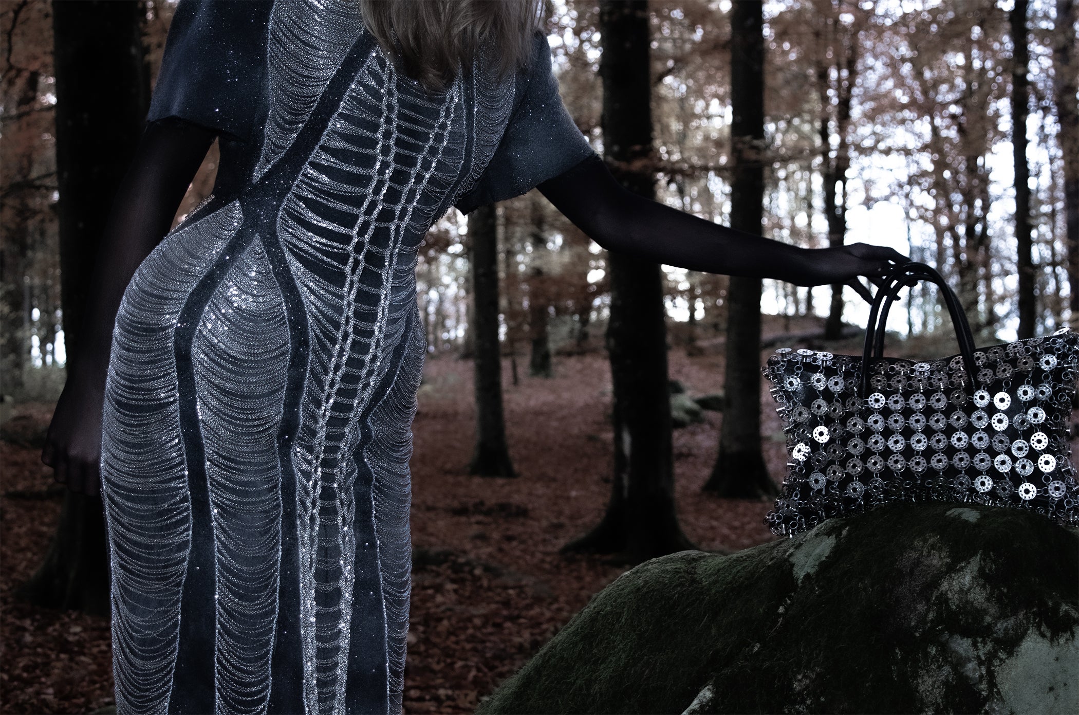 Person in a sequined outfit standing in a forest with a sequined bag.