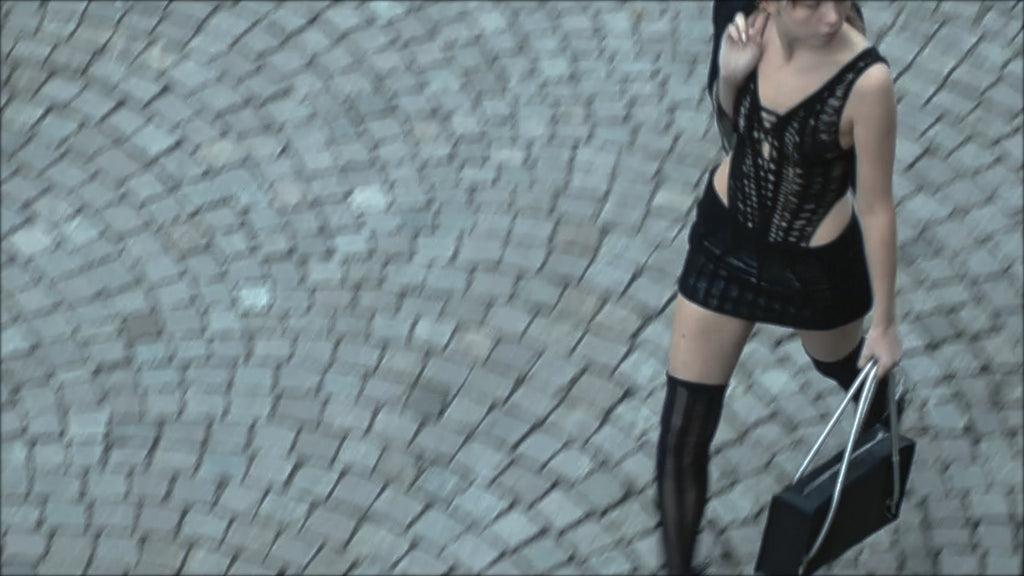 Person in black lace top and skirt holding a handbag on a cobblestone street