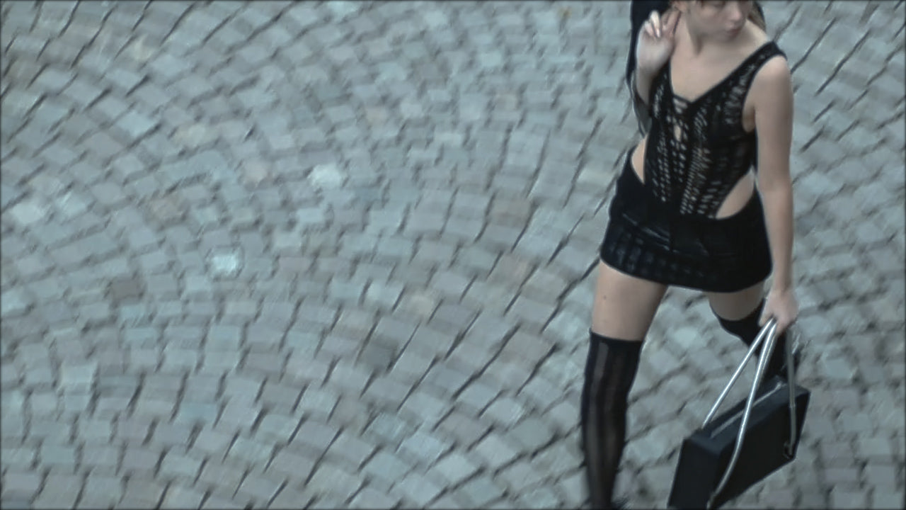 Person in black lace top and skirt holding a handbag on a cobblestone street