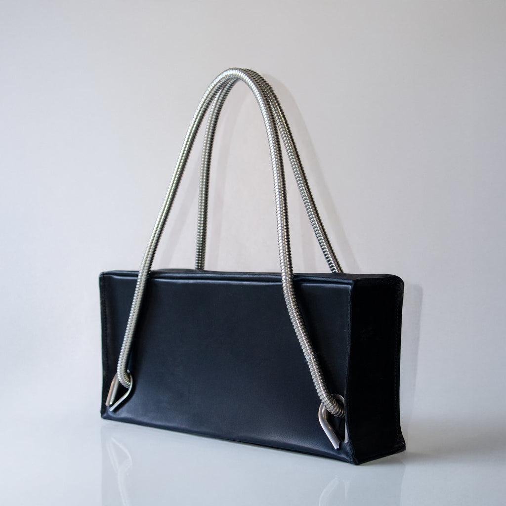 Black leather handbag with silver handles and eyelets on a light gray background