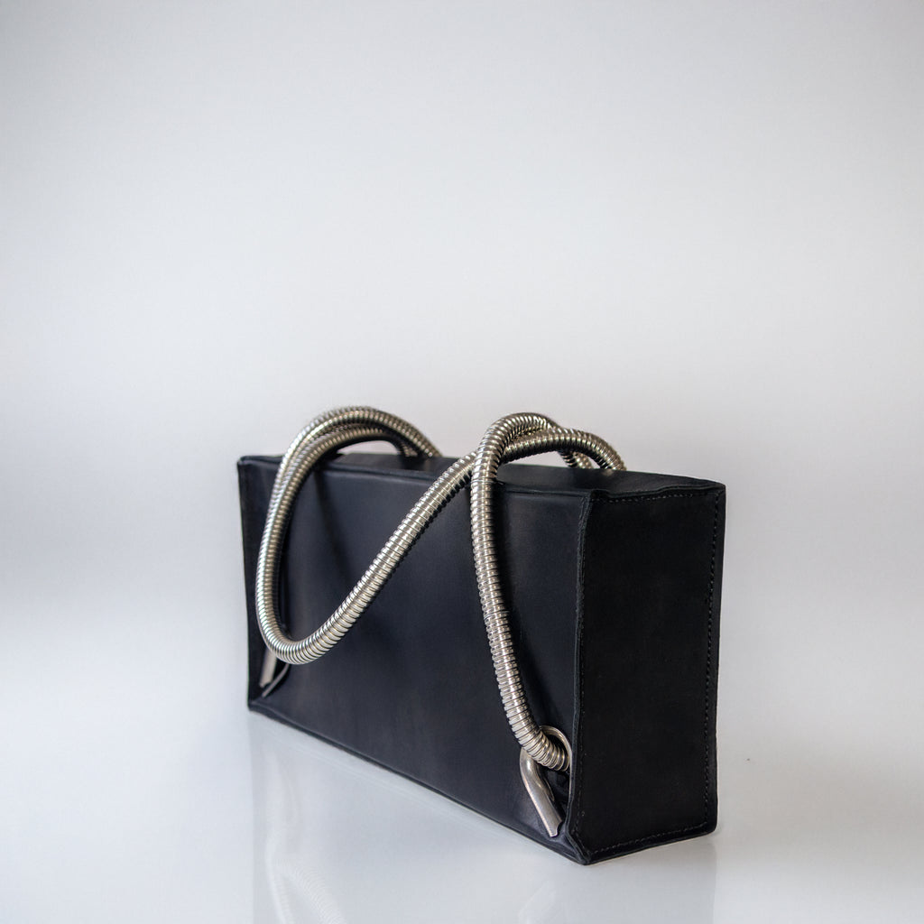Black leather handbag with silver handles and eyelets on a light gray background