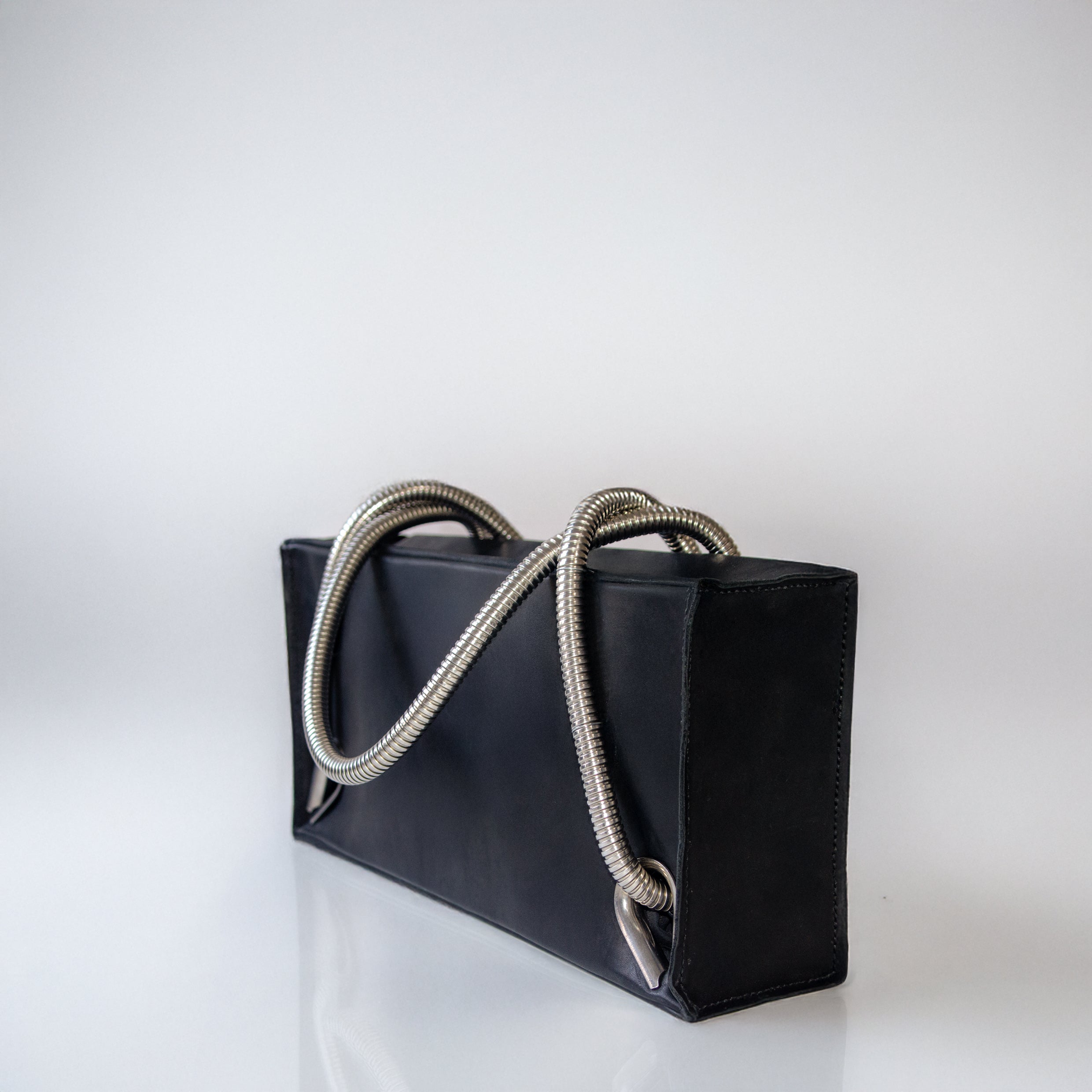 Black leather handbag with silver handles and eyelets on a light gray background